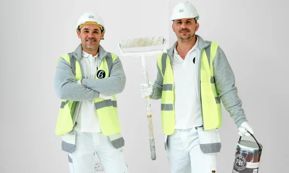 Two Professional Painters With Paint Rollers Standing Next To Each Other In Front Of Freshly Painted White Walls